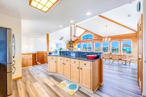 Une cuisine spacieuse avec des meubles en bois, un grand îlot central et une vue sur l’océan grâce à de grandes fenêtres.