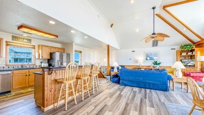A spacious living area with a kitchen, wooden flooring, and a large blue sofa. - Semi-Oceanfront Dog Friendly w/ Pool, Hot Tub, Cargo Lift, Nearby Beach Access (Salvo)
