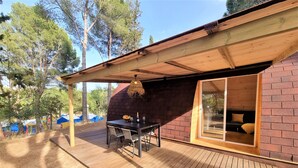 Une terrasse en bois avec une table et des chaises, une porte vitrée donnant sur une pièce et un mur en briques.