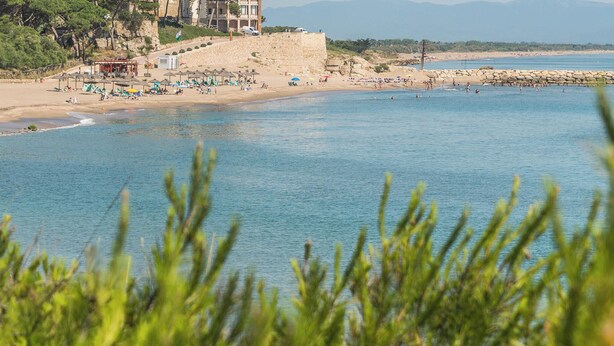 A coastal hotel with a beach view, a stone wall, and a flag on the building. - Nomad Paraiso: Beautiful cozy and familiar bungalow (L'Escala)