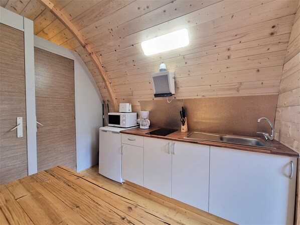 Una cocina compacta con paredes de madera, microondas, cafetera y lavamanos.