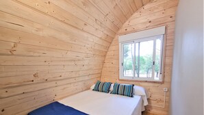 A wooden cabin room with a bed, a window, and a view of trees. - Nomad Paraiso: Beautiful cozy and familiar bungalow (L'Escala)