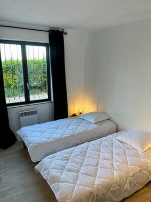 Una habitación con dos camas, una ventana con cortinas, un radiador y una mesita de noche con lámpara.