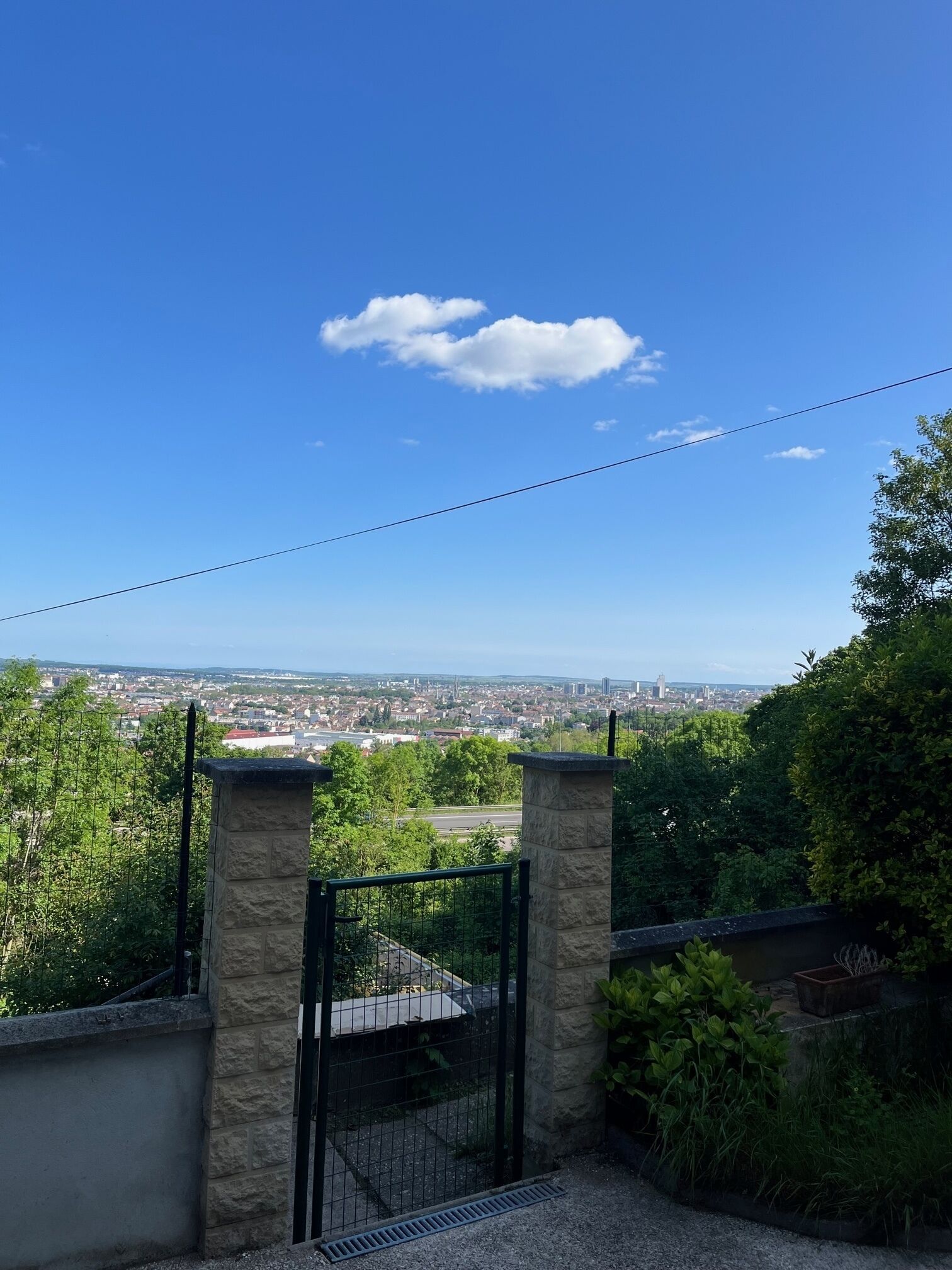 A gated entrance with stone pillars, a view of a cityscape, and a clear blue sky.