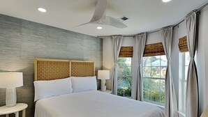 A modern bedroom with a large bed, two bedside lamps, a ceiling fan, and a view of greenery through the windows. - Seaspray | Private Pool + 4 Bikes (Miramar Beach)