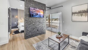 Ein modernes Wohnzimmer mit einem großen Fernseher, einem Holztisch und einem grauen Sofa.