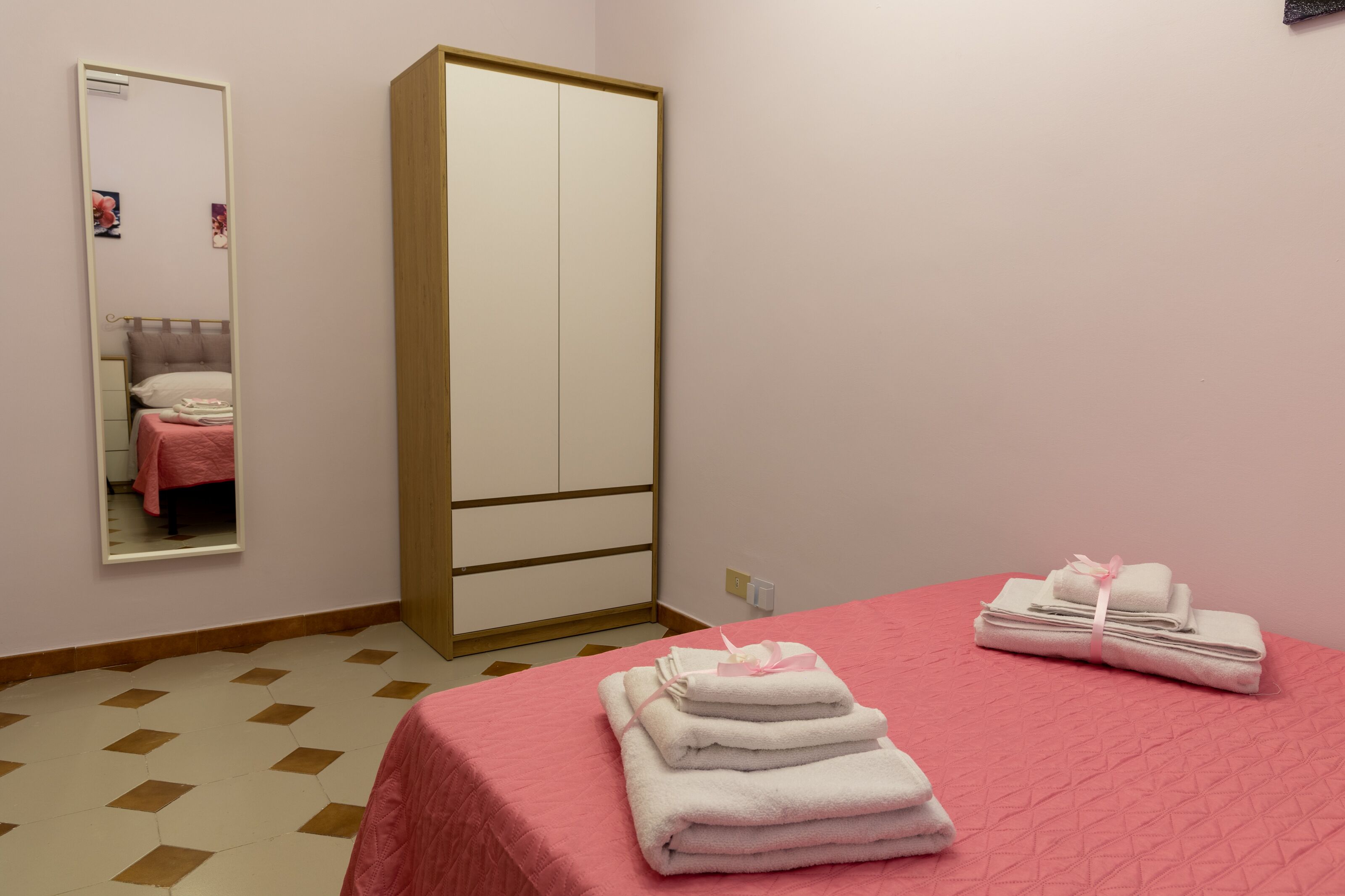 A bedroom with a bed, a wardrobe, a mirror, and a stack of towels.