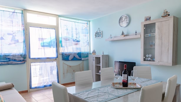 A dining area with a table set for two, a television, and a cabinet with glass doors. - Stella Marina apartment, vacation home in Trapani, a few steps from the sea  (Trapani)