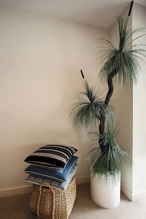 Un coin agrémenté d’une plante en pot, d’un panier en osier et de plusieurs coussins empilés.