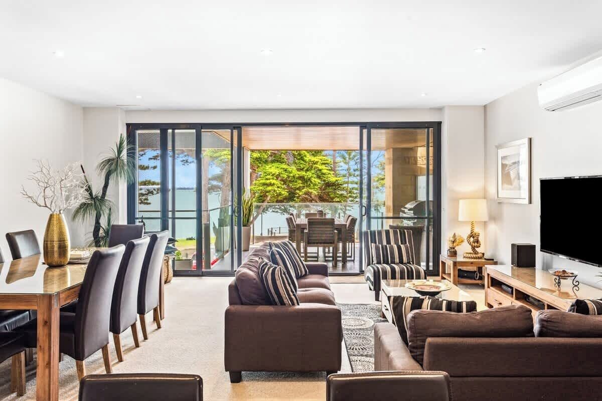 A modern living room with a dining area, large windows, and a flat-screen TV.