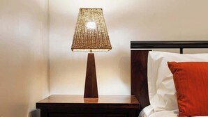 Una cama bien hecha con ropa de cama blanca y naranja, una mesita de noche de madera con una lámpara y un cabecero de madera.