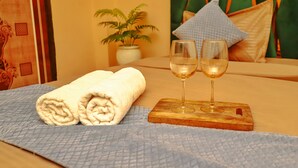 A neatly made bed with two rolled towels and two glasses of white wine on a wooden tray. - Roomshala 059 Sp Lodge (New Delhi)