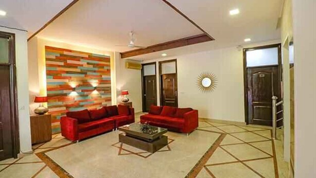 A living room with a modern design, featuring a red sofa set, a coffee table, and a colorful wall. - Roomshala 059 Sp Lodge (New Delhi)
