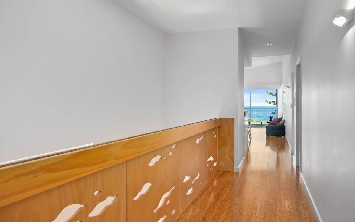 Een moderne hal met een houten leuning, die leidt naar een balkon met uitzicht op zee.