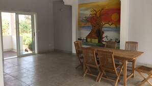 A spacious dining area with a large wooden table and chairs, a mural of a tree and sunset on the wall, and a sliding glass door leading to an outdoor area.