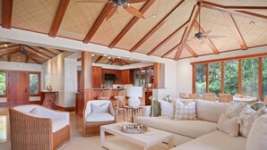 A spacious living area with a high ceiling, large windows, and a kitchen in the background. - Serene 3BR Pakui Estate 131 at Hualalai – Infinity-Edge Pool & Ocean Views (Kailua Kona)