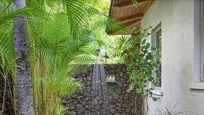A tropical garden with a waterfall, a stone wall, and a potted plant. - Serene 3BR Pakui Estate 131 at Hualalai – Infinity-Edge Pool & Ocean Views (Kailua Kona)
