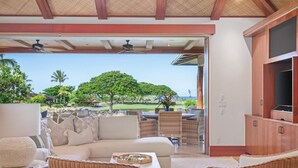 A cozy outdoor seating area with wicker furniture, a sofa, and a television on a wooden cabinet. - Serene 3BR Pakui Estate 131 at Hualalai – Infinity-Edge Pool & Ocean Views (Kailua Kona)