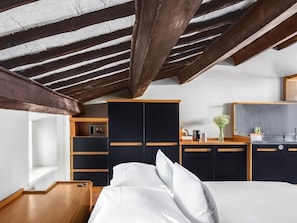 A bedroom with a bed, wooden nightstands, a built-in wardrobe, and a kitchenette area.