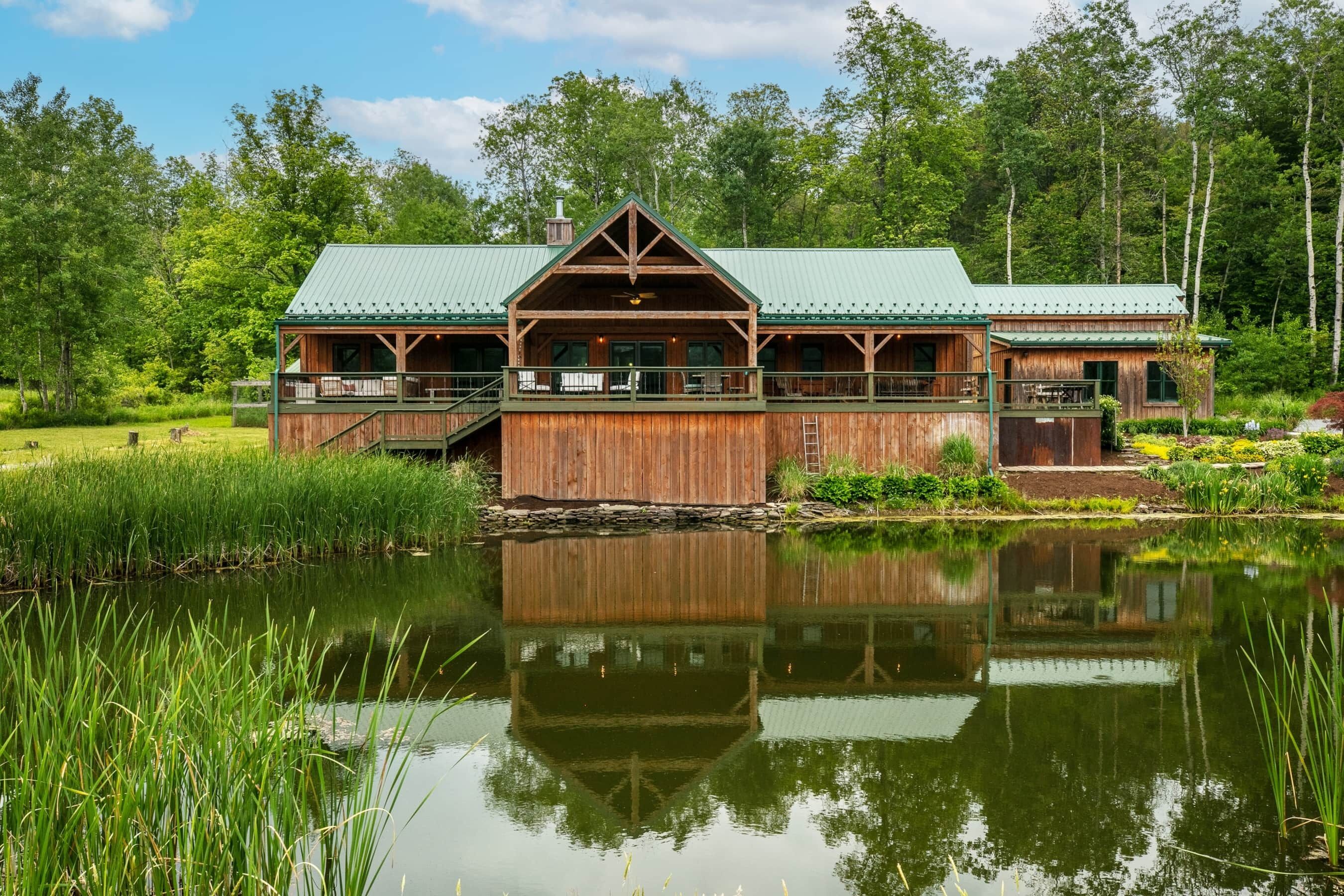A rustic lodge with a green roof, wooden exterior, and a deck overlooking a pond.