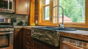 Una cocina con armarios de madera, encimera de granito, pileta de acero inoxidable y ventana con vista a árboles.