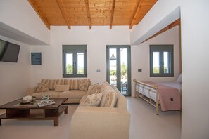 A spacious living room with a wooden ceiling, a sofa set, a bed, and a television mounted on the wall. - Ariadni di Olivio Villa (Zakynthos)