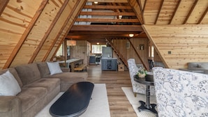 Un acogedor loft con techo de madera, un sofá seccional, una mesa de comedor y una cocina al fondo.