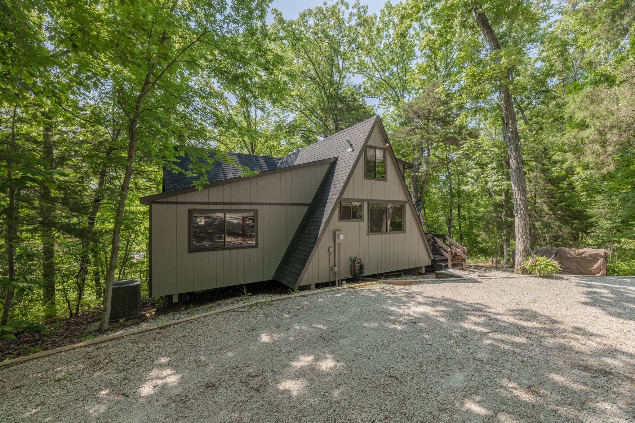 Een chalet met een schuin dak, een veranda en een grindpad, omgeven door bomen.