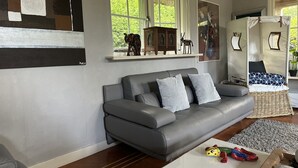 A modern living room with a grey leather sofa, a white coffee table, and a rug. There are windows with a view of greenery outside. - ERMELO Hideaway  (Ermelo)