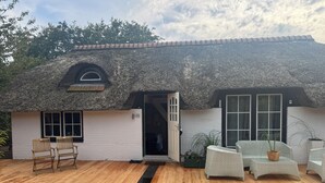 A building with a thatched roof, white walls, and a wooden deck with wicker furniture. - ERMELO Hideaway  (Ermelo)