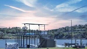 An outdoor seating area with Adirondack chairs and a fire pit, overlooking a lake with a boat slip structure in the background. - Marble Falls Lakefront Paradise w/Fire Pit! (Marble Falls)