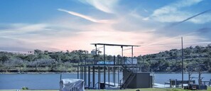 An outdoor seating area with Adirondack chairs and a fire pit, overlooking a lake with a boat slip structure in the background. - Marble Falls Lakefront Paradise w/Fire Pit! (Marble Falls)