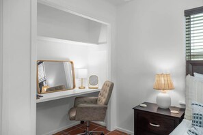 A bedroom with a vanity, a chair, a bedside table with a lamp, and a bed with a white headboard. - A Pecan Retreat-Fire pit- 3 Blocks to Main St! (Fredericksburg)