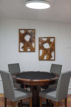 A round table with four gray upholstered chairs, two wall-mounted abstract wooden art pieces, and a recessed ceiling light. - A Pecan Retreat-Fire pit- 3 Blocks to Main St! (Fredericksburg)