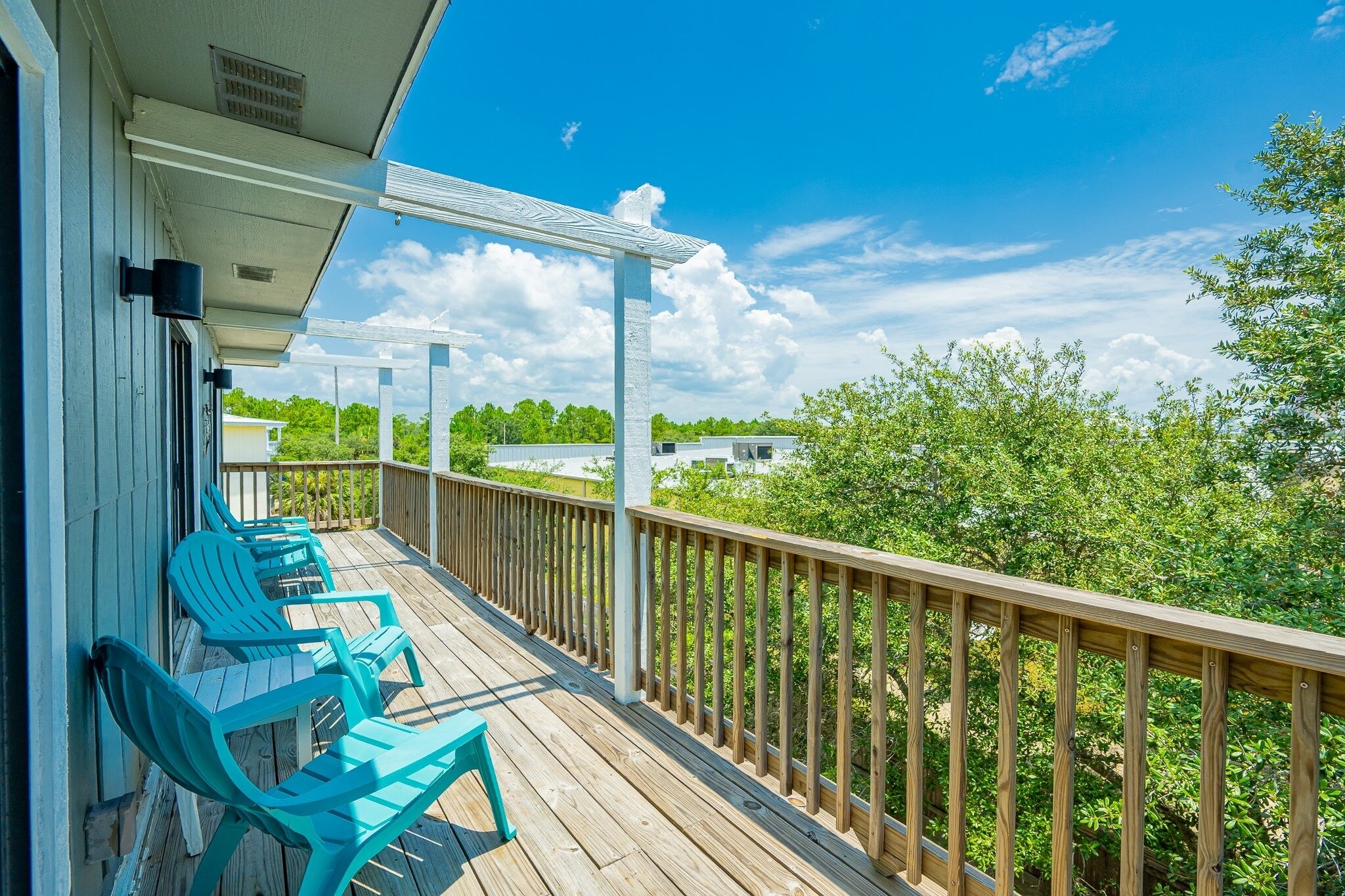 A wooden deck with blue chairs, a railing, and a view of greenery and buildings.