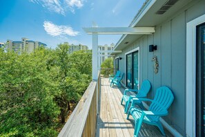 A wooden deck with turquoise chairs, a pergola, and a view of dense greenery and buildings in the background.