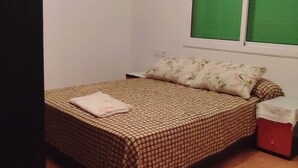 A small, neatly arranged bedroom with a bed, a nightstand, and a window with green blinds. - Appartement Spacieuse et Propre à Louer (Martil)