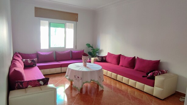 A living room with a sectional sofa, a round coffee table, and a potted plant. - Appartement Spacieuse et Propre à Louer (Martil)