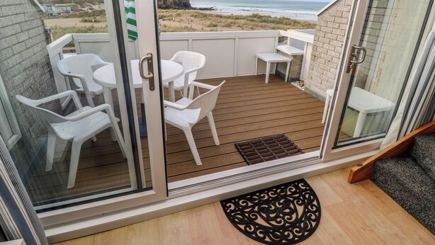 A balcony with a view of the beach and ocean, furnished with white chairs and a small table. - 16 Seaspray (Truro)