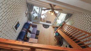 A loft-style living area with a wooden staircase, a ceiling fan, and a view of the outdoors through a sliding glass door. - 16 Seaspray (Truro)