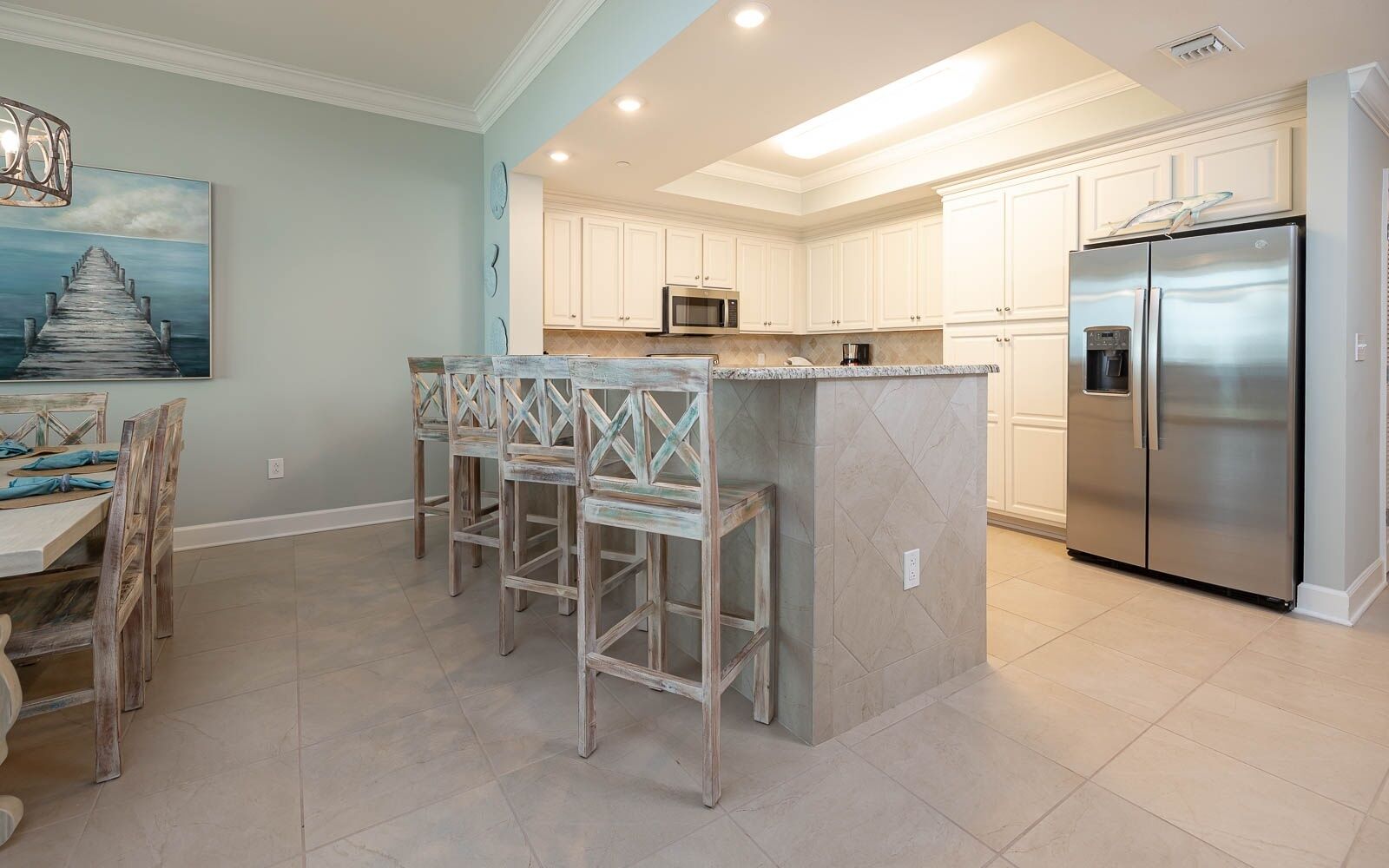 A kitchen with white cabinets, a stainless steel refrigerator, and a dining area with wooden chairs and a table.