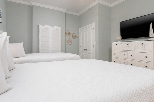 A bedroom with two beds, a dresser, a television, and decorative wall art. - Phoenix Gulf Towers 303 3 Bedroom Condo (Orange Beach)