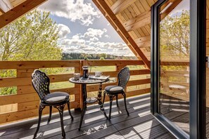 A wooden deck with a table and two chairs, overlooking a green landscape with trees and a cloudy sky. - Buttercup Lodge | The Ridgeway Holiday Let | 2 Beds & Sleeps 4 (Benson)