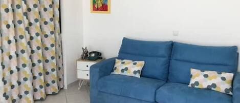 A room with a blue sofa, a white nightstand, a telephone, and a colorful painting on the wall.
