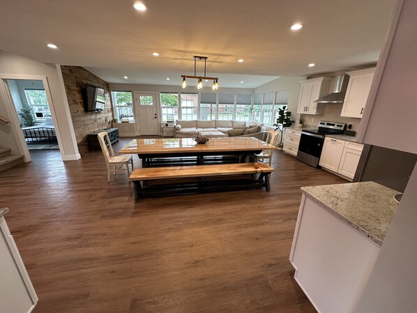 A spacious kitchen with a large wooden dining table, white cabinets, and a modern stove. - Completely remodeled getaway! Walking distance to beach, restaurants and bars (Port Sanilac)