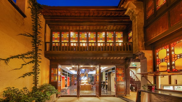 A traditional building with a wooden balcony, large stained glass windows, and a staircase leading to an upper level. - Wuzhen Dream Hotel (Jiaxing)