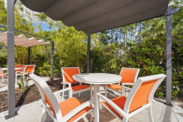 Une terrasse extérieure avec des chaises blanches et orange, une table ronde et un espace abrité.