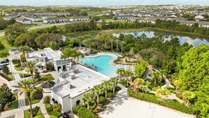 Vue aérienne d’un quartier résidentiel avec une piscine entourée de verdure et une plage de sable blanc.