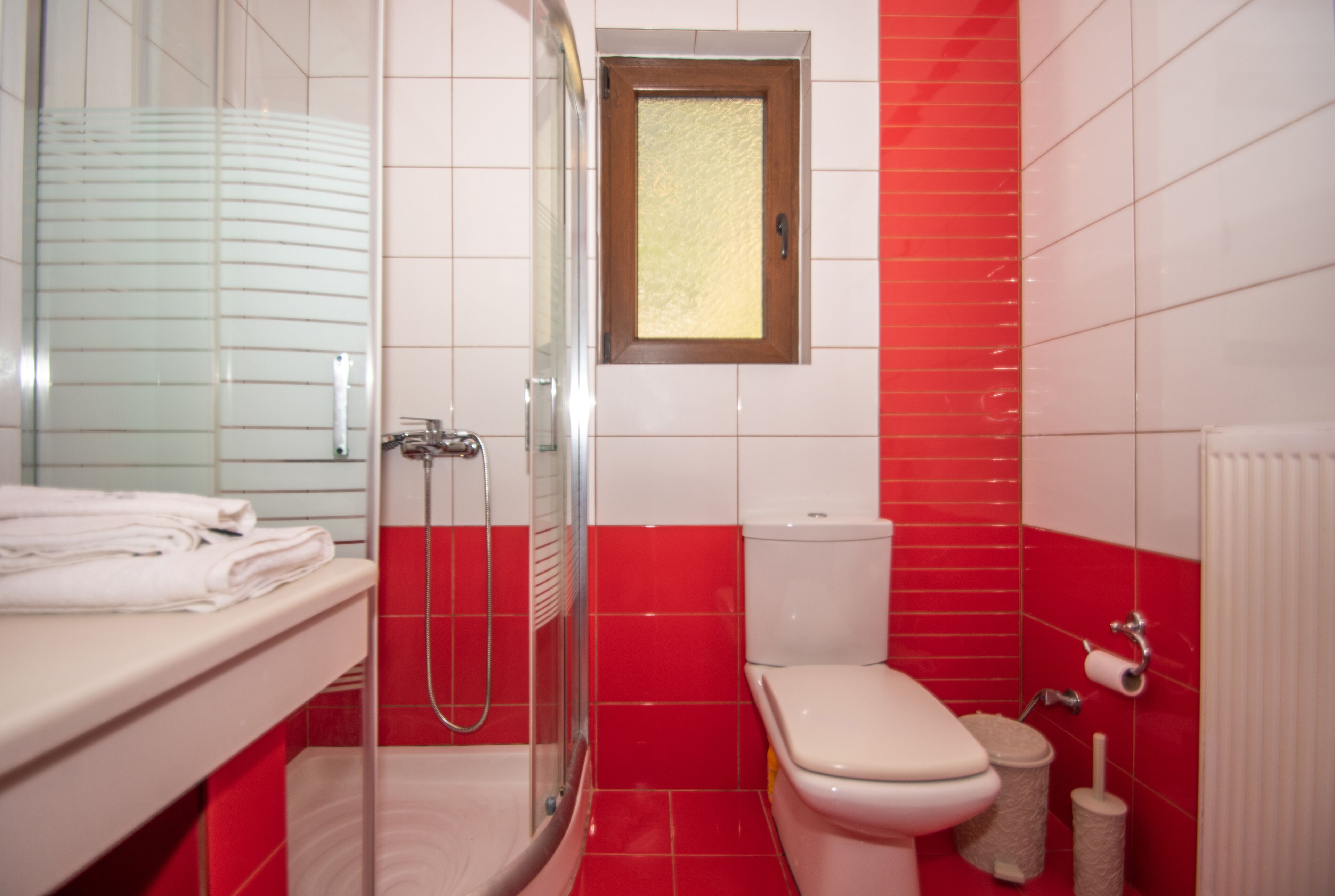 A bathroom with a glass shower enclosure, a toilet, and a sink with a towel rack.