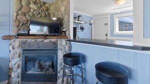A kitchen with a stone fireplace, a flat-screen TV, and a bar area with stools. - Romantic, Walk to town and beach, Private (ArchView) (Long Beach)